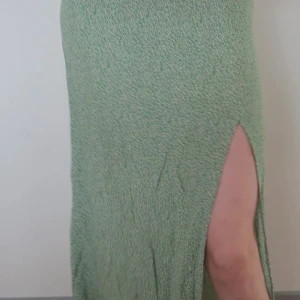 Grön långkjol med slits - Snygg grön långkjol med en elegant slits på sidan. Perfekt för sommarens fester eller en avslappnad dag ute. Kjolen har ett diskret mönster som ger den en unik touch. Passar bra för både vardag och festliga tillfällen.