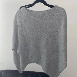 Grå poncho - Säljer en supermysig grå poncho i mjukt material. Perfekt för kyliga höst- och vårdagar. Den har en lös passform och är lätt att slänga över en tröja eller blus för extra värme. Enkelt och stilrent plagg som passar till det mesta! 🩶