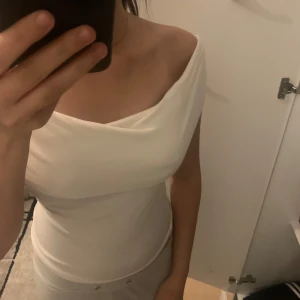 Vit offshoulder topp - Säljer en stilren vit offshoulder topp som är perfekt för sommaren. Den har en tight passform och är tillverkad i ett mjukt och bekvämt material. Toppen är enkel men elegant och kan lätt matchas med olika outfits.