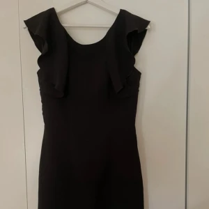 Svart klänning med volangdetaljer - svart klänning med volangdetaljer vid ärmarna. Super snygg och bekväm, knappt använd.