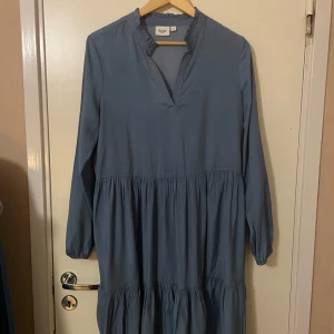 Klänning från Saint Tropez - Säljer en blå klänning från Saint Tropez i storlek M. Klänningen har långa ärmar och en avslappnad passform med volanger.