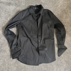 Svart långärmad skjorta - Säljer en stilren svart långärmad skjorta. Perfekt för både vardag och fest! Skjortan har knappar hela vägen ner och en klassisk krage. Den är i bra skick och passar till alla tillfällen. 🖤