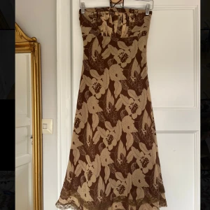 Brun mönstrad bandeauklänning med snören - Så fin klänning köpt second hand men aldrig använd av mig, väldigt bra skick. Går att göra till bandeau om man viker in banden