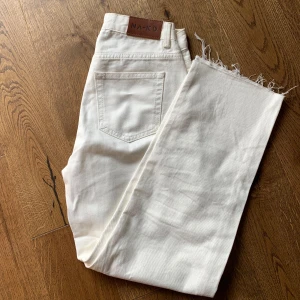 Vita jeans från NA-KD - Säljer ett par snygga vita jeans från NA-KD. De är högmidjade och har en straight passform. Jeansen har en klassisk femficksdesign. Perfekta för både vardag och fest! De har en rå kant vid bensluten för en trendig look.