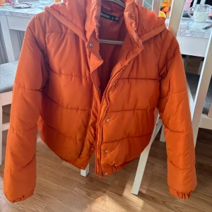 Orange pufferjacka från Missguided - Säljer en supercool orange pufferjacka från Missguided. Den är perfekt för höst och vinter med sin varma och vadderade design. Jackan har en dragkedja framtill och en mysig huva. Den är i fint skick och redo att hålla dig varm och stilren i kylan. Passar perfekt för en casual look eller när du vill sticka ut lite extra!