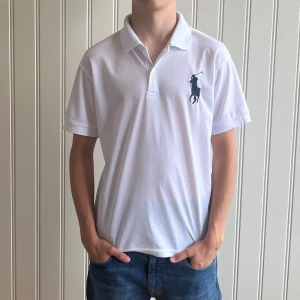 Vit pikétröja från Ralph Lauren - Säljer en klassisk vit pikétröja från Ralph Lauren. Den har en broderad logga på bröstet och en siffra '3' på ärmen. Perfekt för en stilren look. Tröjan är i bra skick och passar till både vardag och fest.
