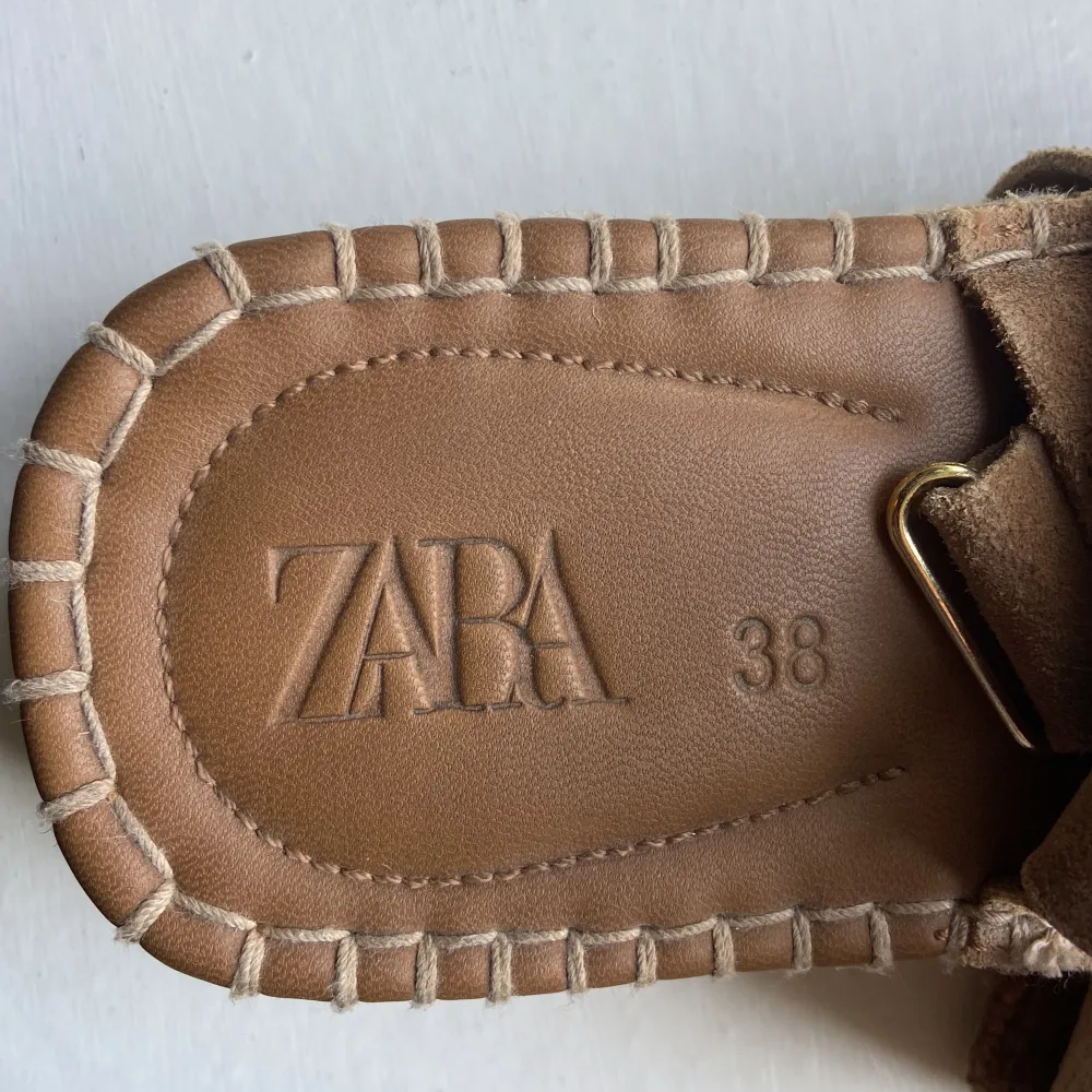 Säljer ett par snygga och bekväma sandaler från Zara i storlek 38. De är i en fin beige färg med en stilren design. Sandalerna har en platåsula med flätad detalj och justerbara remmar i mocka med guldfärgade spännen. Perfekta för sommaren!. Skor.