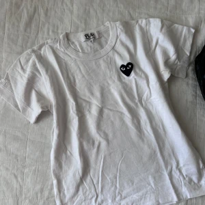 Vit t-shirt med hjärtdetalj från PLAY - Säljer en stilren vit t-shirt från PLAY commes des garcons med ett svart hjärta på bröstet. Perfekt för en casual look och passar till allt! T-shirten är i bra skick och redo för nya äventyr.