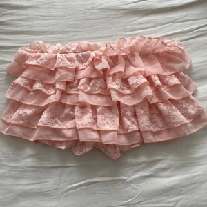 Rosa volangkjol - Säljer en superfin rosa kortkjol med volanger. Kjolen har flera lager av volanger som ger en söt och lekfull look. Den har shorts under och är i strl L, men passar även mindre storlekar. väldigt stretchigt material. Aldrig använd 