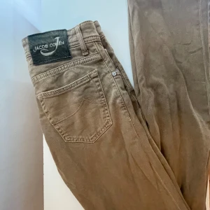 Beige/ljusbruna Jeans från Jacob Cohën - Säljes: Exklusiva byxor i nyskick! Använda endast ett fåtal gånger och i fantastiskt skick – inga märken, hål eller andra defekter.  Storlek: Italiensk 30 (motsvarande cirka 30/32 eller 30/33 i svensk storlek). Modellen är slim-fit. Kom dm för frågor