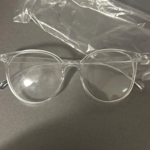 Transparenta glasögon - Säljer ett par stilrena och moderna transparenta glasögon. De har en rund form som ger en klassisk look och är perfekta för både vardag och fest. Glasögonen är i nyskick och kommer med ett skyddande fodral.