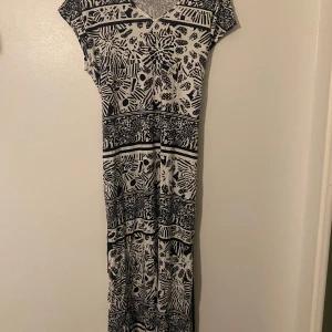 Svartvit mönstrad klänning från Noom - Säljer en superfin svartvit klänning från Noom i storlek M. Den har ett coolt mönster med blommor och ränder, perfekt för både vardag och fest. Klänningen är kortärmad och har en v-ringad hals. Materialet känns mjukt och skönt mot huden. Passar perfekt till sommaren eller våren!