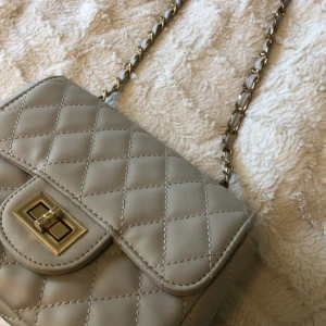 Beige handväska med gulsdetalier - Säljer denna väska i fint skick, men det finns lite defekter vid sidan av väskan som visas på sista bilden. Den har guldiga detaljer med tre stycken mindre fack och ett stort💞jag har gjort en knut för att få kortare snöre men det går att reglera🫶🏼