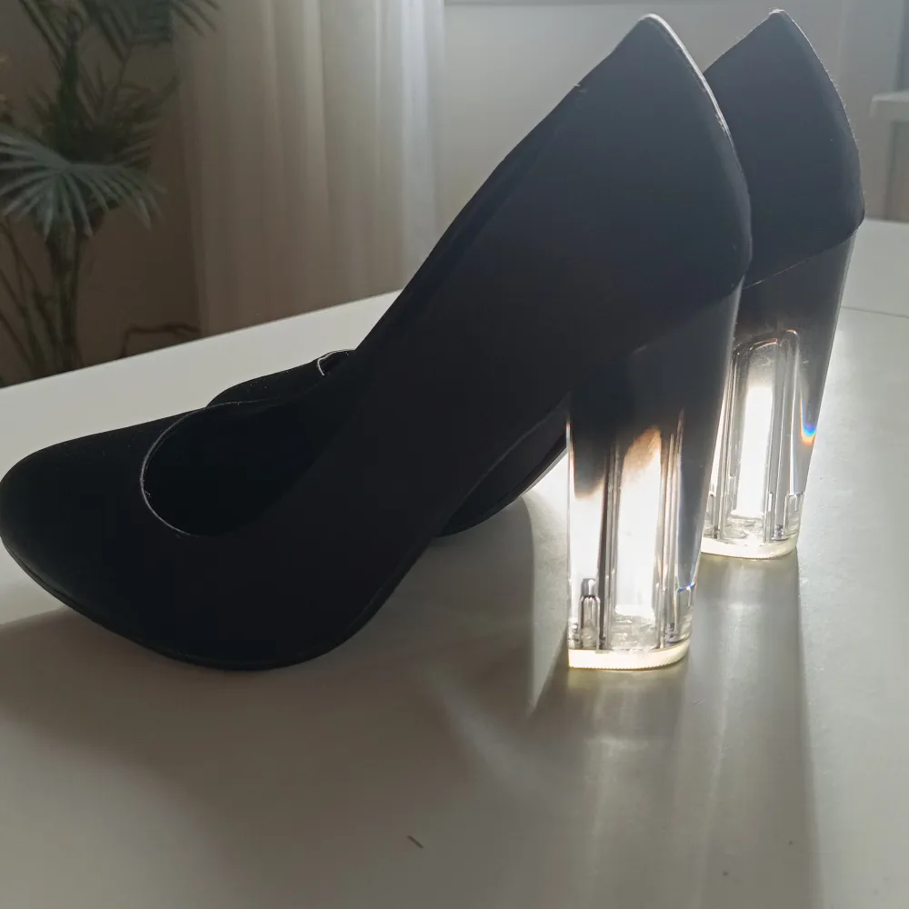 Säljer ett par eleganta svarta pumps med en unik transparent klack. Skorna är i nyskick och har en stilren design som passar perfekt för festliga tillfällen. Materialet är mjukt och bekvämt, vilket gör dem sköna att bära hela kvällen. . Skor.