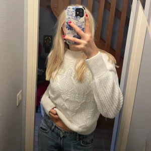 Vit stickad tröja - Säljer en supermysig vit stickad tröja som är perfekt för kyliga dagar. Den har ett snyggt flätmönster och långa ärmar. Tröjan är i nyskick och passar perfekt till jeans för en avslappnad look. Perfekt för höst och vinter!