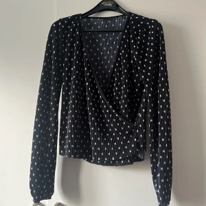Svart omlottopp med prickar från Gina Tricot - Säljer en superfin svart omlottopp från Gina Tricot i storlek XS. Toppen har ett prickigt mönster i vitt och långa ärmar. Perfekt för både vardag och fest! 🖤