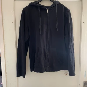 Svart hoodie från 157 - Säljer en svart hoodie från 157 i storlek XL. Den har en dragkedja framtill och en klassisk huva med snören. Perfekt för en avslappnad stil och passar till alla tillfällen. Skön och enkel att matcha med andra plagg. Hör av dig vid intresse!