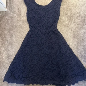 Mörkblå spetsklänning julklänning nyårsklänning - Säljer en superfin mörkblå spetsklänning i storlek 158/164. Klänningen har ett vackert blommigt mönster och en omlott-design i ryggen. Perfekt för festliga tillfällen! 💙