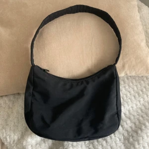 Svart handväska från Ginatricot  - Säljer en stilren svart axelväska. Perfekt för vardagsbruk med en praktisk dragkedja upptill. Väskan har en enkel design som passar till alla outfits. Perfekt för dig som vill ha en smidig och snygg väska att bära med sig.