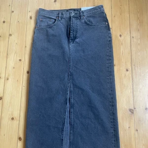 Grå jeanskjol från & Other Stories - Säljer en snygg grå jeanskjol från & Other Stories. Kjolen har en rak passform och är i ett klassiskt denimtyg. Perfekt för både vardag och lite mer uppklädda tillfällen. Den har en mid waist och är utan stretch, vilket ger en stilren look. Passar perfekt till höst- och vårgarderoben!