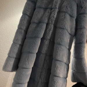 pälsjacka - Säljer en supermjuk och fluffig grå pälsjacka. Perfekt för att hålla sig varm och stilren under kalla dagar. Jackan har långa ärmar och en elegant design som passar både till vardags och fest. Den är i nyskick och redo för en ny ägare!