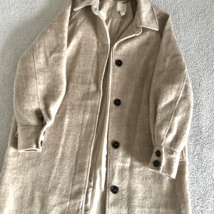 Beige lurvig kappa med knappar - Superfin beige lurvig kappa från H&M med stora svart/bruna knappar. Perfekt för höst och vinter! Den har långa ärmar och två fickor framtill. Kappan är i nyskick och har en klassisk stil som passar till det mesta. Perfekt för att hålla sig varm och snygg under kyliga dagar. Endast använd en gång, utan anmärkningar och i nyskick. 🧸Storlek XS men väldigt oversize och passar även S utan problem.