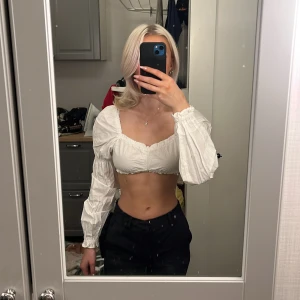 Vit croppad blus från H&M Divided - Säljer en superfin vit croppad blus från H&M Divided. Den har långa ärmar och en söt volangdetalj vid ärmslut och nederkant. Perfekt för sommaren eller en festlig kväll! 💫