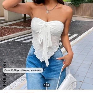 Vit axelbandslös topp med knyt - Säljer en superfin vit axelbandslös topp från SHEIN. Den är perfekt för sommaren med sitt lätta och luftiga material. Toppen har en söt knytning framtill som ger en extra touch. Passar perfekt till jeans eller kjol för en chic look!