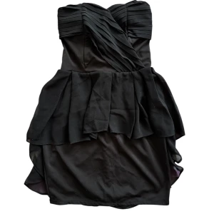 Svart axelbandslös klänning - Snygg svart axelbandslös klänning med volangdetaljer och omlott-design. Perfekt för en kväll ute eller en speciell tillställning. Den har en elegant och stilren look som verkligen sticker ut⭐️