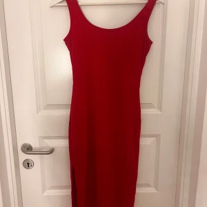 Röd ribbad klänning - Snygg röd ribbad klänning med en smickrande passform. Klänningen är ärmlös och har en slits som ger en extra touch. Perfekt för att sticka ut i mängden. Passar bra till både vardag och speciella tillfällen.