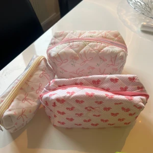 Söta quiltade necessärer med rosett-mönster - Tre quiltade necessärer i vitt med rosa detaljer. Två av dem har ett mönster av rosa rosetter och en har ett mönster av rosa och gröna blommor. Alla har dragkedja i matchande färg. Perfekta för att organisera dina småsaker! 150kr/st 