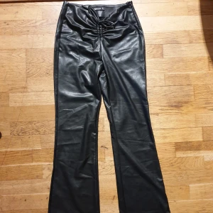 Svarta skinnbyxor från FB Sister - Snygga svarta skinnbyxor (skinnimitation) från FB Sister med en unik knytning framtill. Byxorna har en högmidjad design och en bootcut-stil som ger en trendig look. Perfekta för att ge din outfit en edgy touch.