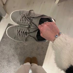 Gråa sneakers med snörning - Säljer ett par stilrena grå sneakers i mocka med snörning. Skorna har en vit sula och vita detaljer vid hälen. Inte alls använda och smutsen går att torka bort vid intresse! Storlek 40