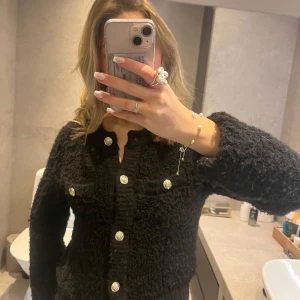 Svart kofta med knappar - Snygg svart kofta med dekorativa knappar framtill. Koftan har en texturerad yta och långa ärmar, man får med en extra knapp🥰