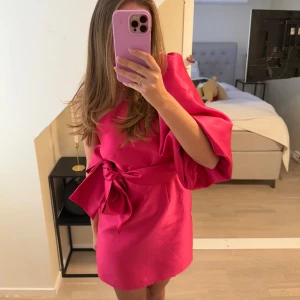 Rosa one-shoulder klänning med knytband - Snygg rosa klänning med en one-shoulder design och ett elegant knytband i midjan. Klänningen har en kort längd och voluminösa ärmar som ger en trendig look. 💞🥰