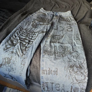 Jeans med tryck - Unika jeans med coolt tryck av skelett och text i svart på ljusblå denim. Byxorna har en loose passform och är perfekta för en edgy stil, vida byxben. Mått: Längd: 107 cm, midja: 80 cm, höft 122 cm och lår 71 cm