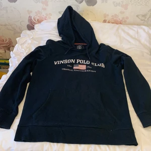 Mörkblå hoodie från Vinson Polo Club - Säljer en snygg mörkblå hoodie från Vinson Polo Club med tryck på bröstet. Tröjan har en klassisk känguruficka och justerbar huva med dragsko. Perfekt för en avslappnad stil.