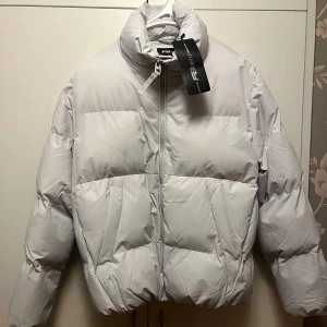 Vit pufferjacka från NewYorker - Säljer en snygg vit pufferjacka från NewYorker. Jackan har en hög krage och dragkedja framtill. Perfekt för kyliga dagar med sin vadderade design som håller dig varm. Märket är New Yorker och storleken är M (passar även S). Passar perfekt för vintern!