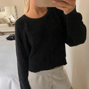 Svart stickad tröja med dragkedja - Säljer en svart stickad tröja med långa ärmar och en cool dragkedjedetalj på sidan. Perfekt för en avslappnad stil. Tröjan har en ribbad struktur och en croppad passform.