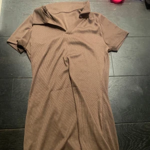 Brun ribbad klänning - Säljer en stilren brun ribbad klänning med korta ärmar och en v-ringad krage. Perfekt för en avslappnad look. Passar bra till både sneakers och klackar. 👜