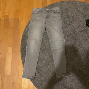 Jack & Jones jeans - Snygga grå jeans från Jack & Jones i en klassisk slim fit. De har en midwaist design och är tillverkade i bomull. Perfekta för en avslappnad stil med fem fickor och knappgylf. Strl är 164cm/14y