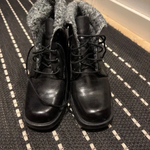 Svarta boots med grått foder - Snygga svarta boots med snörning och grått stickat foder. Perfekta för kyligare dagar med en robust klack och stilren design. Passar bra till både jeans och kjol.