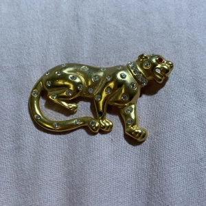 Guldfärgad leopardbrosch med stenar - Elegant guldfärgad brosch i form av en leopard, dekorerad med glittrande stenar, en sten saknas.