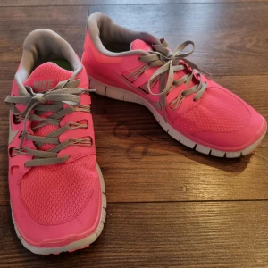 Nike rosa löparskor Nike Free Run NYA - Nya snygga rosa Nike löparskor med grå snörning och vit sula. Perfekta för en sportig look, bekväma för träning såväl som vardagsbruk. De har en delad sulan för skönt steg. De har också en luftig meshdesign för extra komfort. Nike Free Run. Storlek: US 8,5, UK 6, EUR 40.