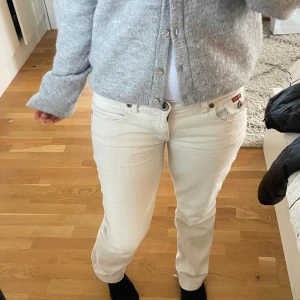 Beige/vita jeans - Snygga beige jeansbyxor med klassisk femficksdesign och knappgylf. Byxorna har en normal passform och är perfekta för en avslappnad stil. De är tillverkade i ett slitstarkt material som ger en bekväm känsla hela dagen.
