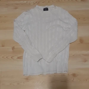 Vit stickad tröja från Iconic Sport - Säljer en stilren vit stickad tröja från Iconic Sport. Tröjan har ett klassiskt flätmönster och är tillverkad i 100% bomull. Perfekt för kyligare dagar med sin långärmade design. Passar bra till både jeans och kjol.