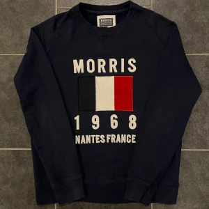 Mörkblå sweatshirt från Morris - Snygg mörkblå sweatshirt från Morris med tryck av fransk flagga och texten 'Morris 1968 Nantes France'. Tillverkad i en mjuk bomulls- och polyesterblandning. Perfekt för en avslappnad stil.