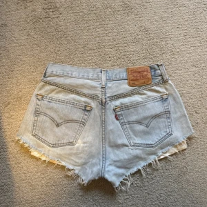 Ljusa jeansshorts från Levi's - Säljer ett par ljusa jeansshorts från Levi's. I den populära modellen 501. De har en klassisk femficksdesign och fransiga kanter för en avslappnad look. Perfekta för sommardagar! 🕶️. Storlek S