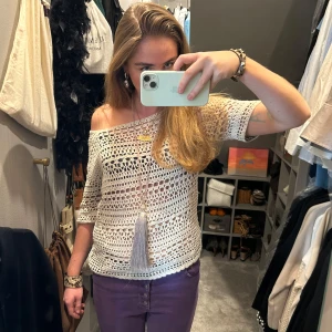 Vit virkad offshoulder topp - Säljer en snygg vit virkad offshoulder topp med trekvartsärm. Toppen har en luftig design och en dekorativ tofs framtill. Perfekt för en avslappnad och stilren look.
