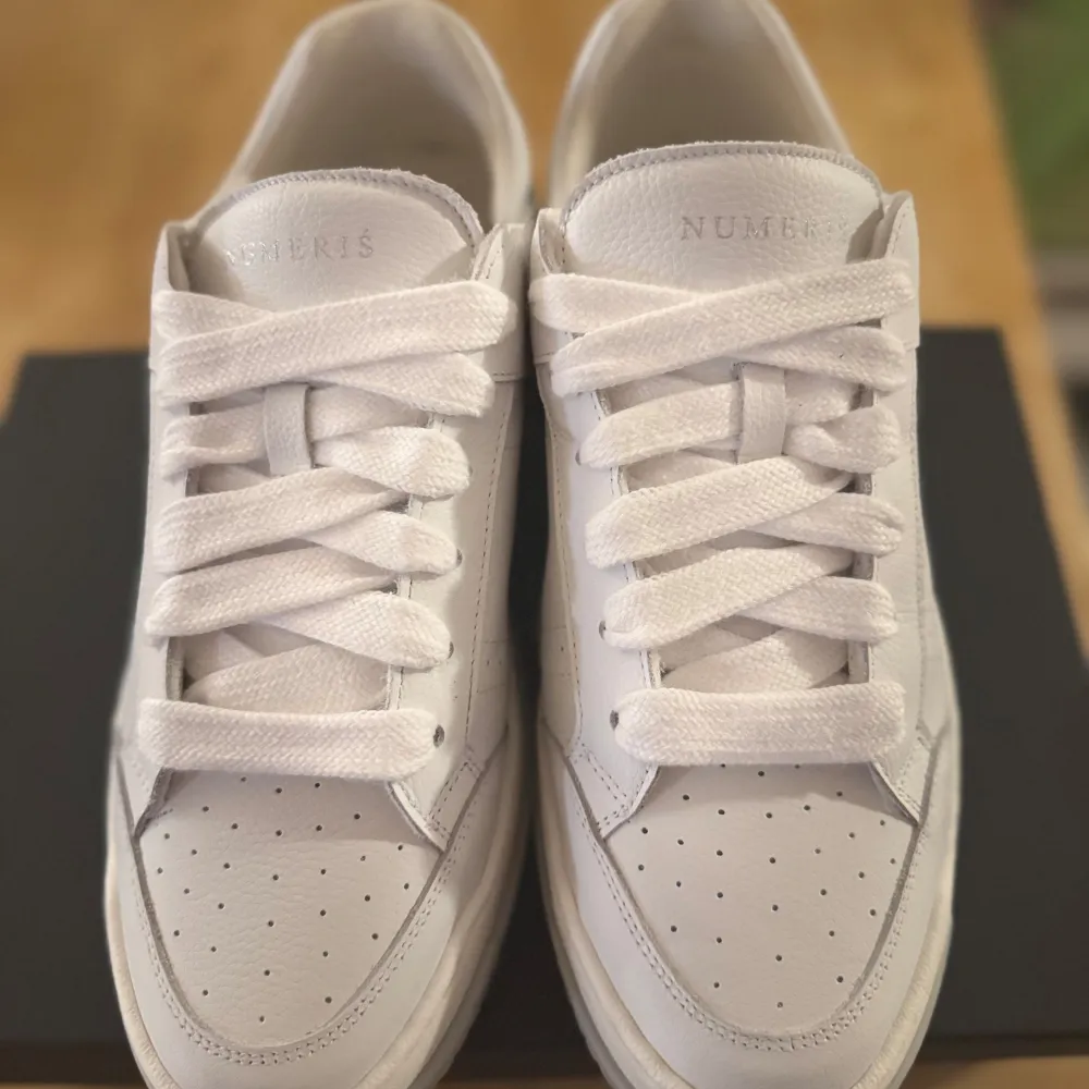 Snygga vita sneakers från Numeris med klassisk design och bred snörning. Skorna har en stilren look med perforerade detaljer på ovansidan och en robust sula med märkets logotyp undertill. Perfekta för en stilren vardagslook. box ingår . Kengät.